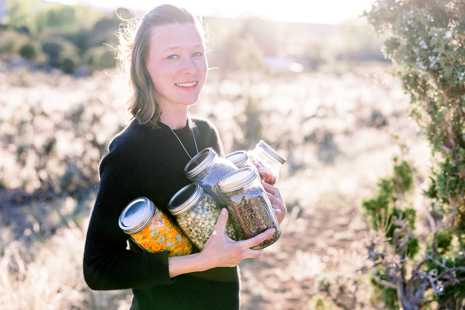 Dr. Shayna Powell holding jars of dried herbs in a Colorado field at sunrise
